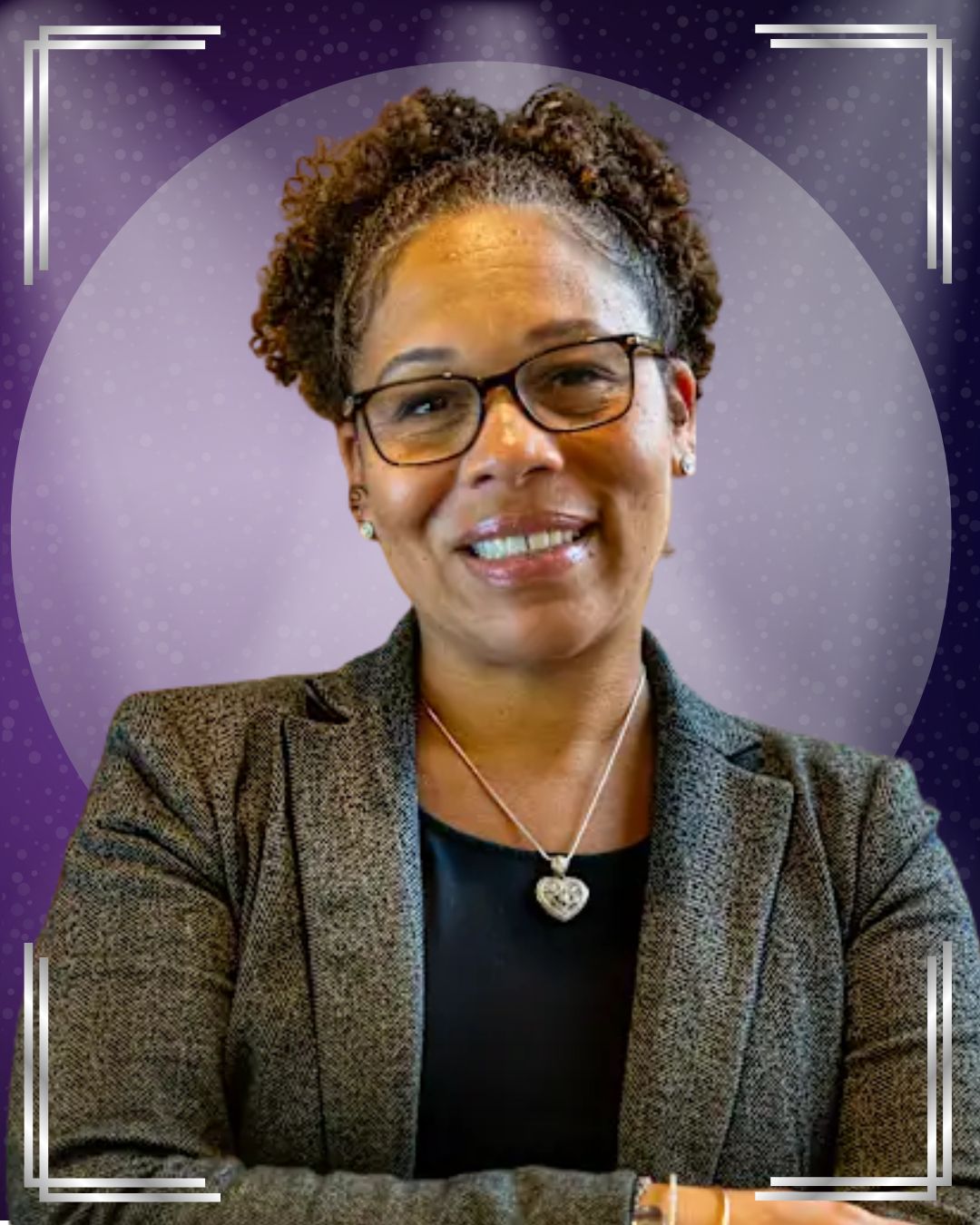 A smiling person wearing glasses, a gray blazer, and a black top, standing against a softly lit purple background with a circular border pattern
