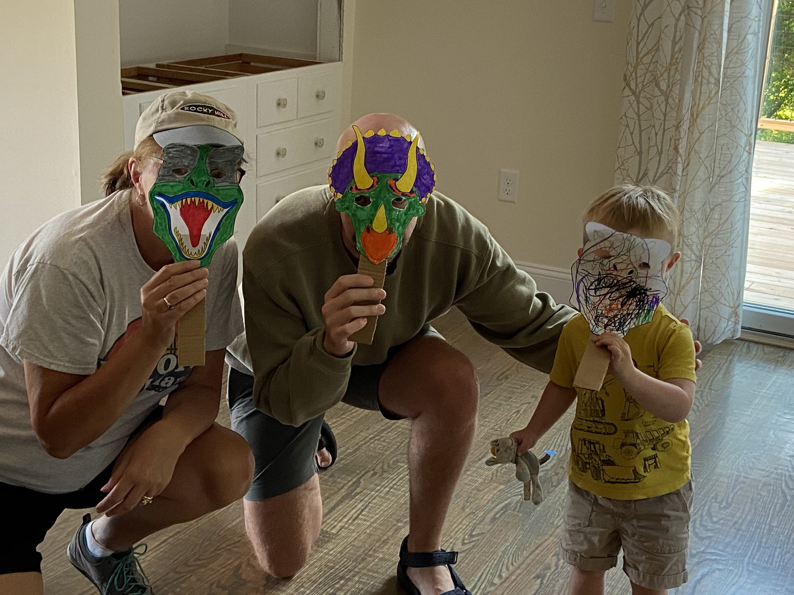 Two adults and one child hold up dinosaur masks over their faces
