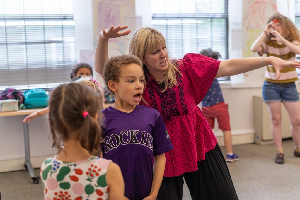 Teaching artist with arms open and a big expression on their face encourage a student to do the same.