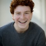 Young boy smiling with ginger hair and blue eyes, wearing a navy sweater.