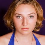 A girl with blonde hair and hazel eyes wearing a blue shirt.