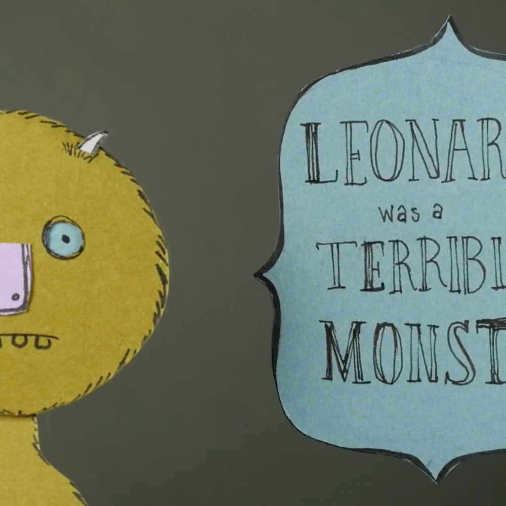 A handwritten-style title card features a simple, friendly yellow monster illustration on the left and stylized text on the right. The monster has round, light blue eyes, a lavender rectangular nose, small pointy white ears or horns, and a few chunky teeth peeking out from a small mouth. To the right, a baby-blue plaque-shaped sign reads in uneven, hand-drawn letters: 
