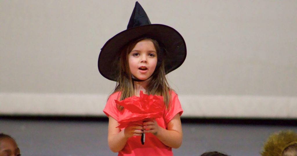 3 A child in a black witches cap holds a red paper flower.