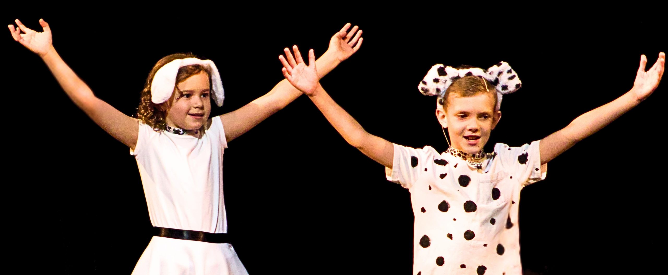 Two students dressed as dalmatians hold up their hands in a joyful pose.