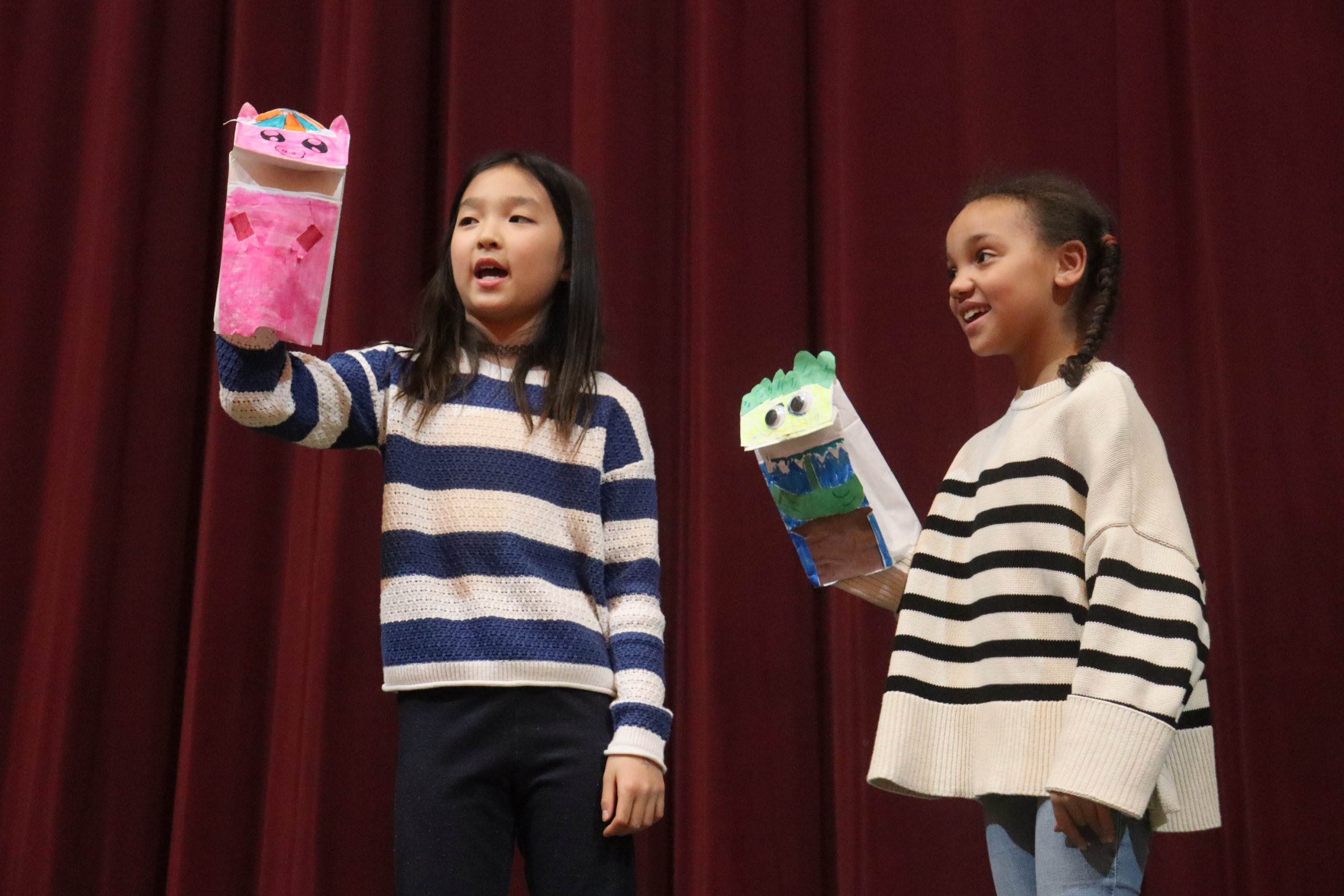 feb-2025-education-landing-page Two students hold up colorful paper bag puppets.