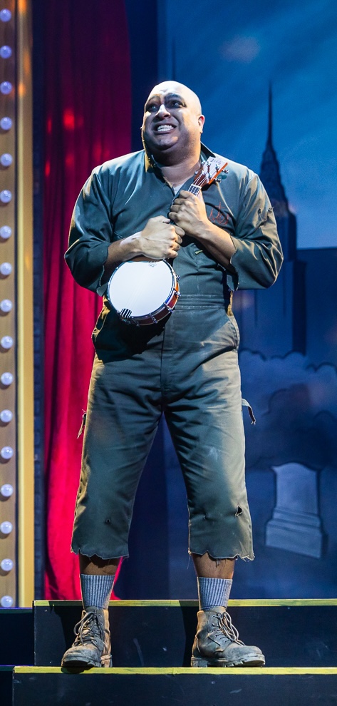 fester-the-addams-family A bald man in a rugged jumpsuit gleefully holds onto a banjo.