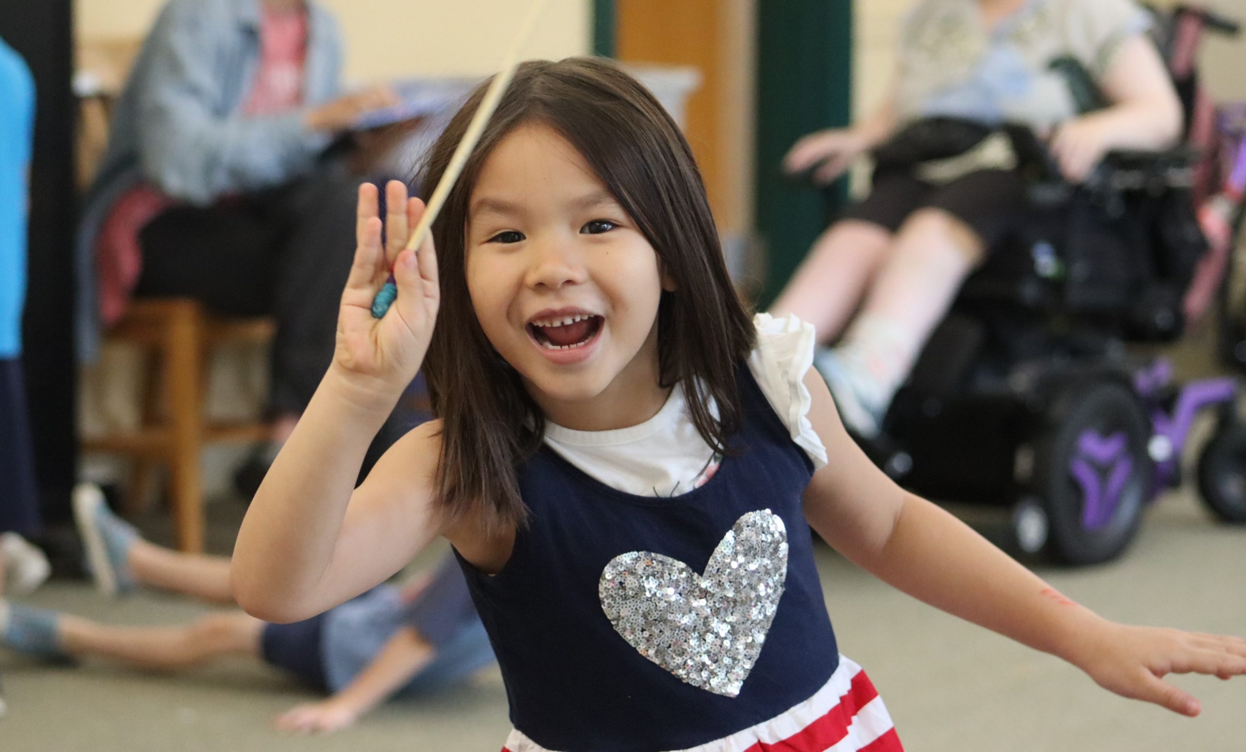 summer-2026-landing-image A child with a large smile, whimsically holds up a pencil