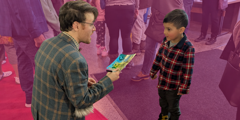An actor is handing a playbill to a young audience member